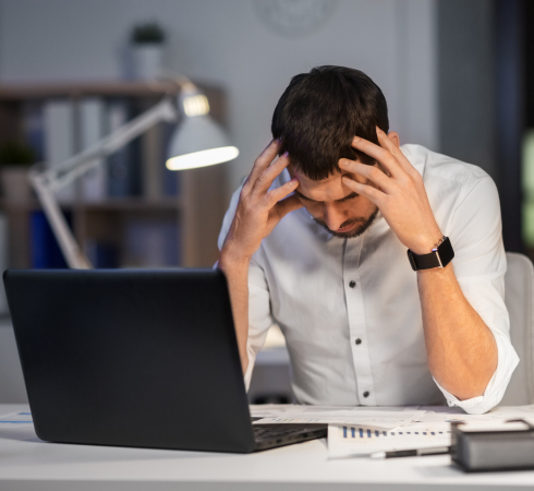 Stressed man holding his head in front of a laptop